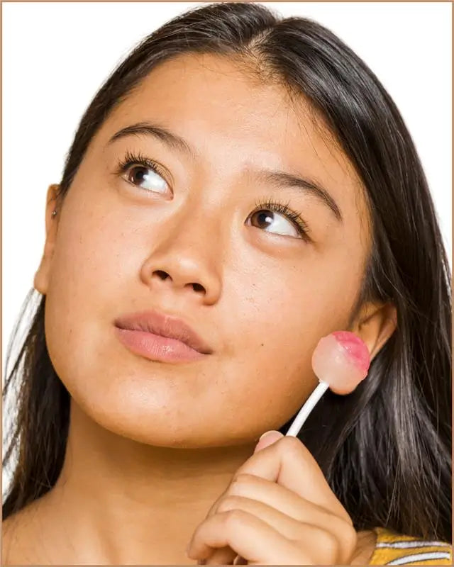 Woman applying pink lip balm to her lips with a white stick.